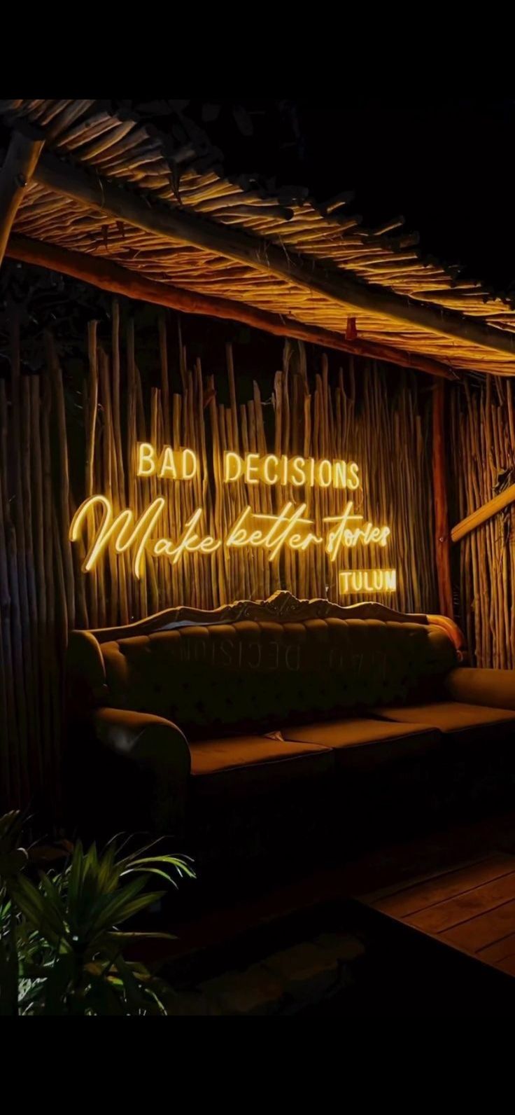 a couch sitting under a neon sign in front of a bamboo wall with writing on it