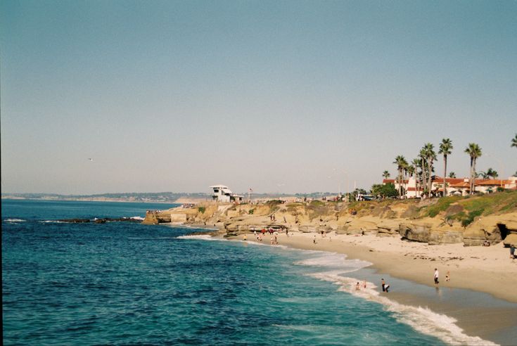 people are walking on the beach by the water