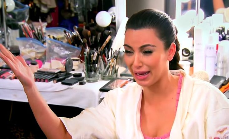 a woman with her hand up in the air while sitting at a table full of makeup brushes