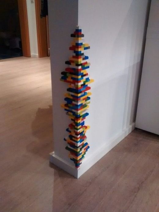 a tall building made out of legos on top of a hard wood floor next to a white wall