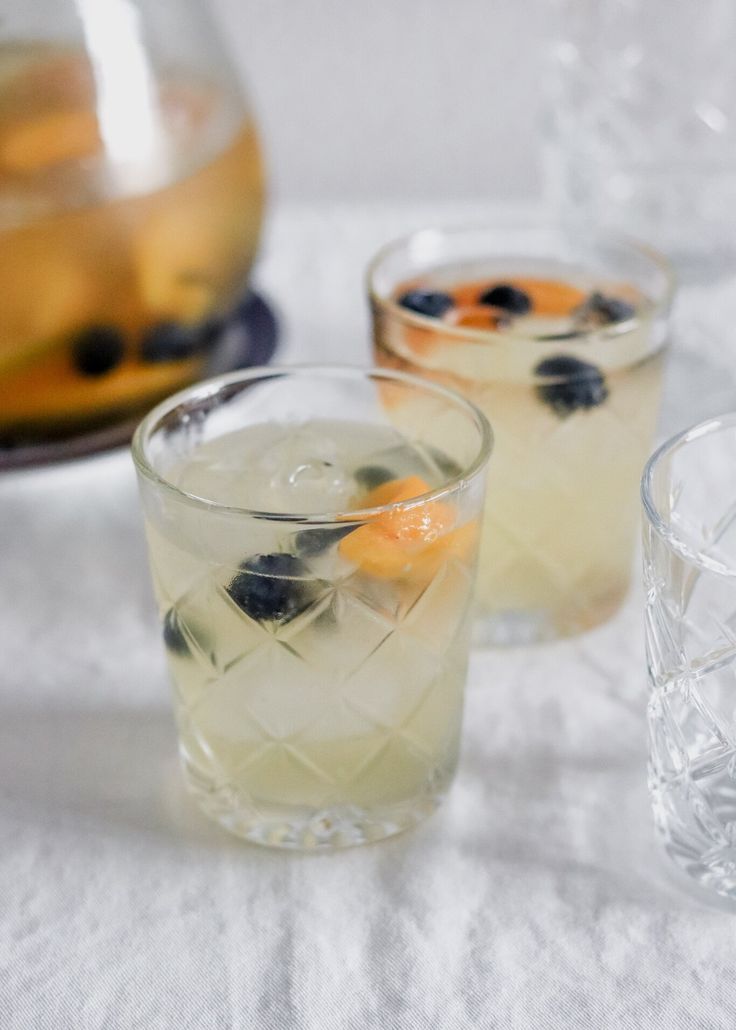 two glasses filled with drinks sitting on top of a white tablecloth covered table cloth