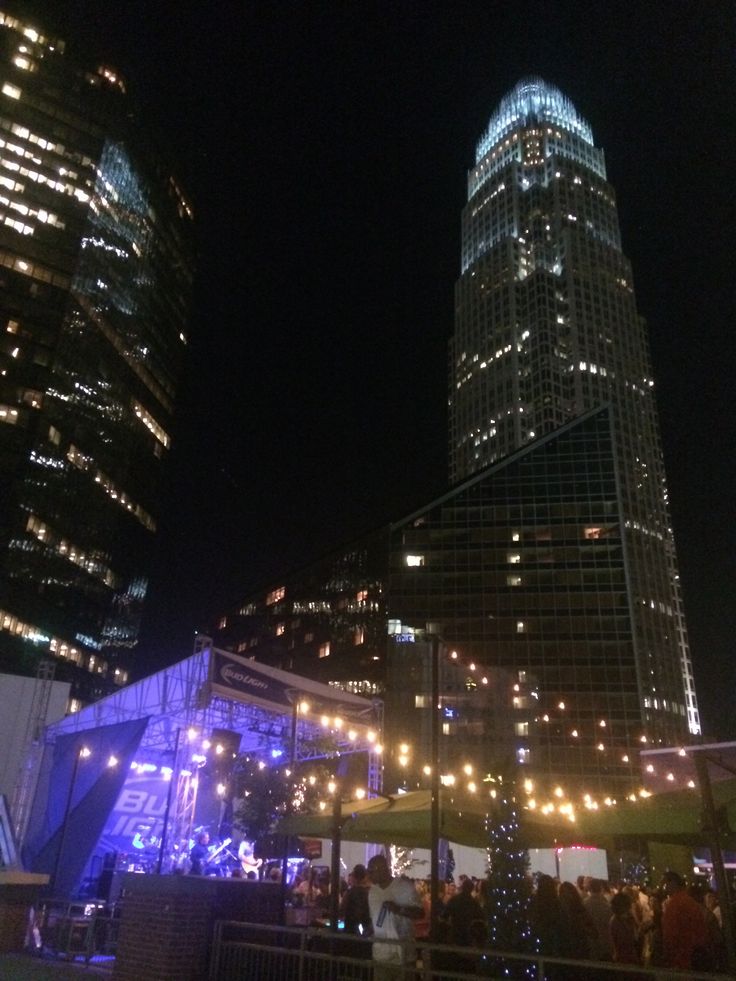 people are gathered outside at night in front of tall buildings with christmas lights on them