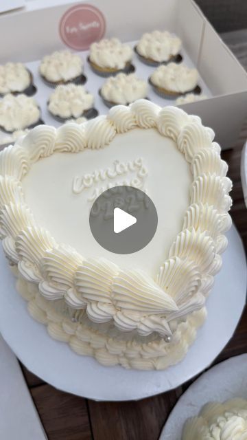 a heart shaped cake with white frosting in a box next to cupcakes