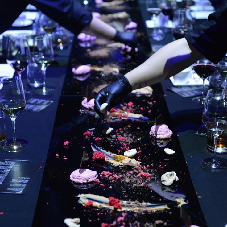 several people are serving desserts at a long table with wine glasses on the side