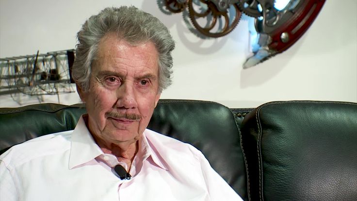 an older man is sitting on a green leather couch with his hands in his pockets