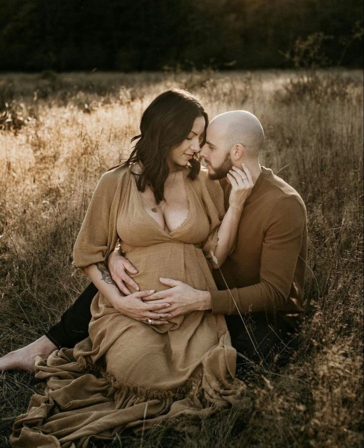 a pregnant couple cuddles in the tall grass