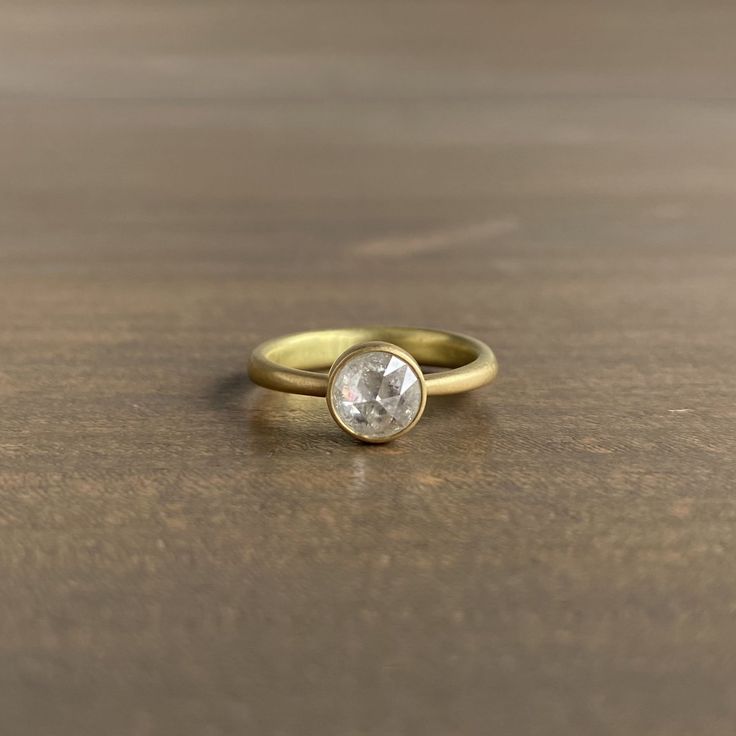 a yellow gold ring with an oval shaped diamond on the center, sitting on a wooden surface