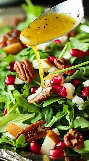 a salad with dressing being poured onto it and topped with apples, pecans, cranberries, and nuts