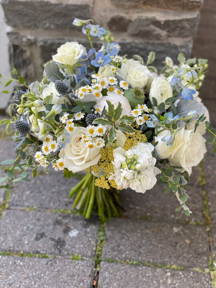 a bouquet of white and blue flowers is sitting on the ground next to a brick wall