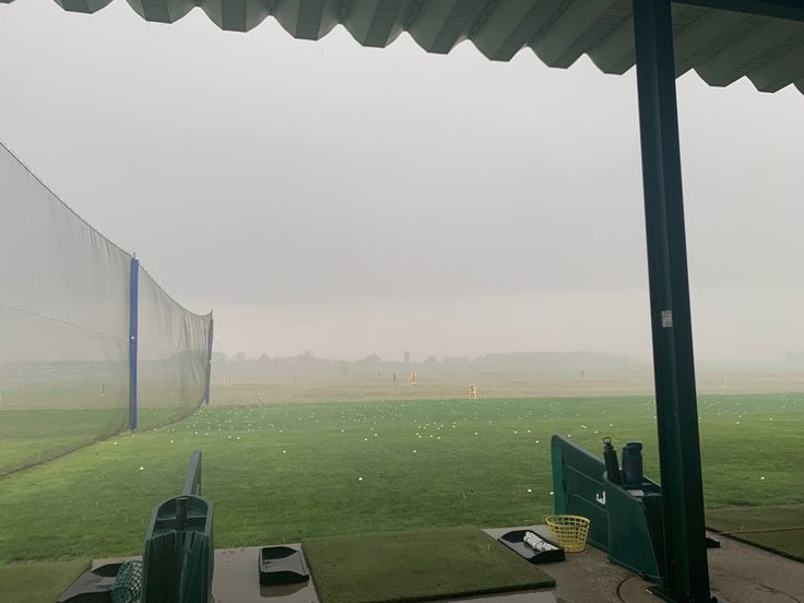 an empty baseball field in the rain with grass on the ground and fence around it