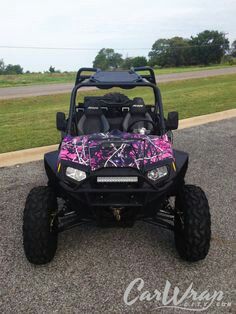 a pink and black vehicle parked on top of a parking lot next to a field