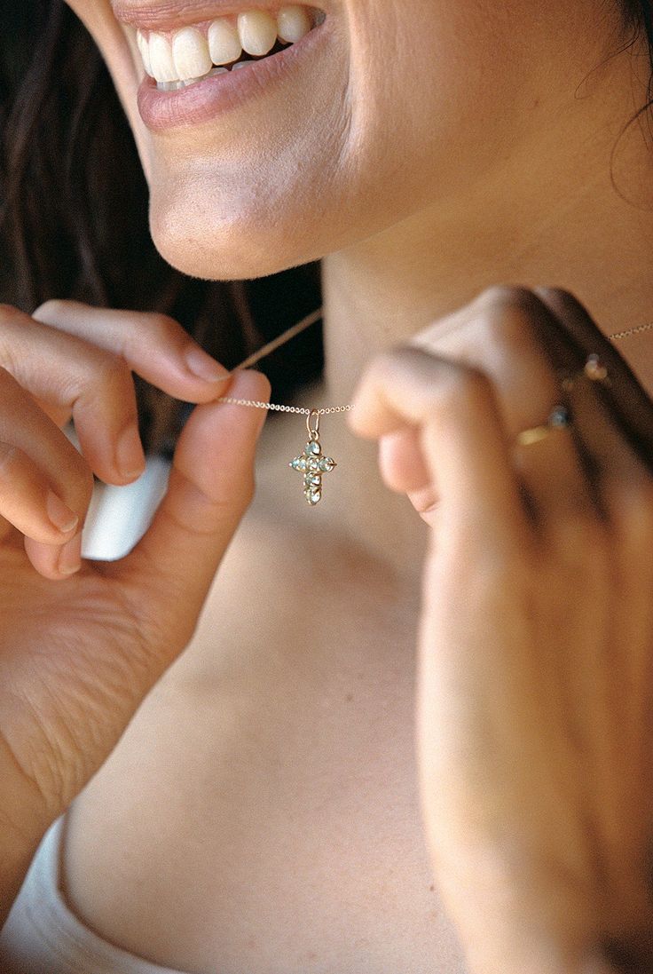 a woman smiles as she adjusts her necklace with a toothbrush in her hand