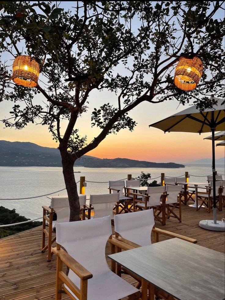 an outdoor dining area overlooking the water at sunset with chairs and umbrellas set up