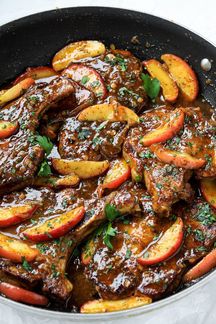 a skillet filled with meat and apples on top of a white tablecloth covered table