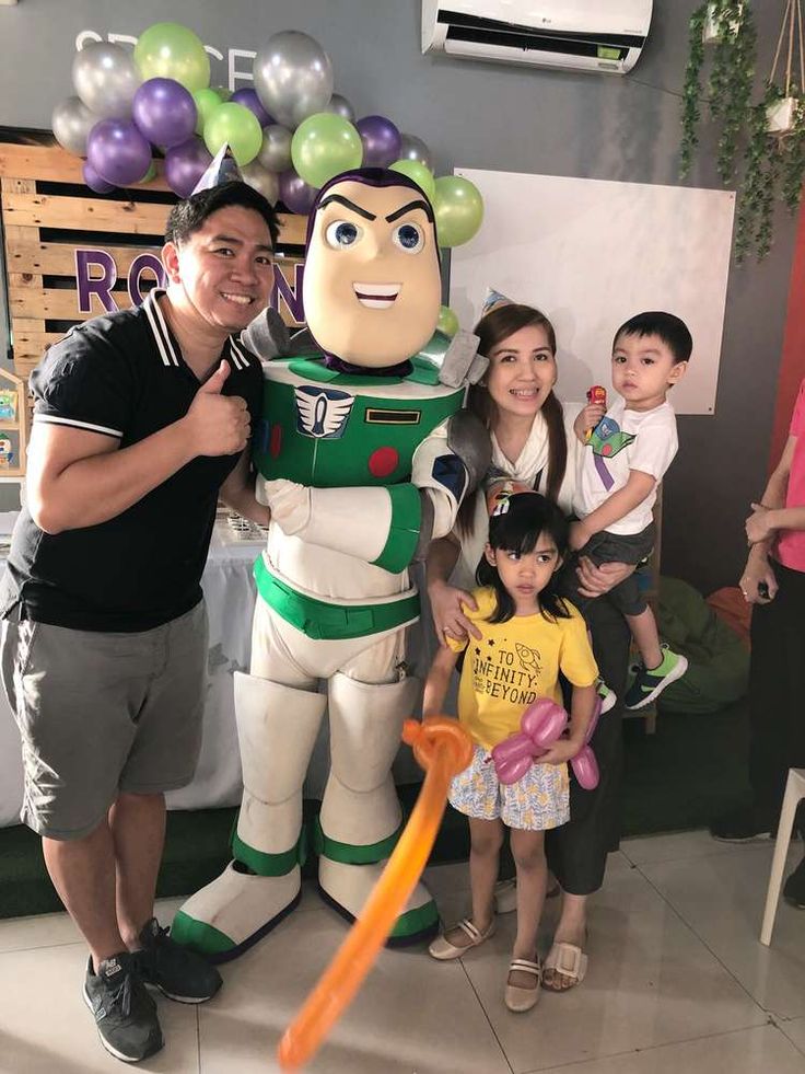 a man and two children standing next to a toy buzz lightyear with balloons in the background