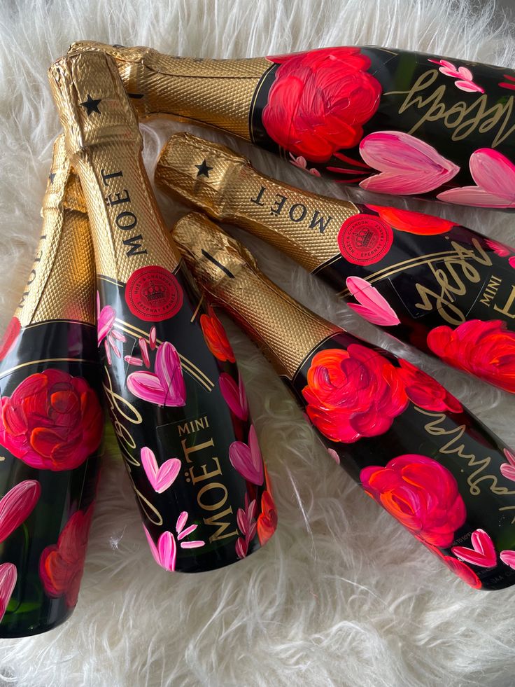 four black and gold decorated wine bottles with pink flowers on them sitting on a white furnishing