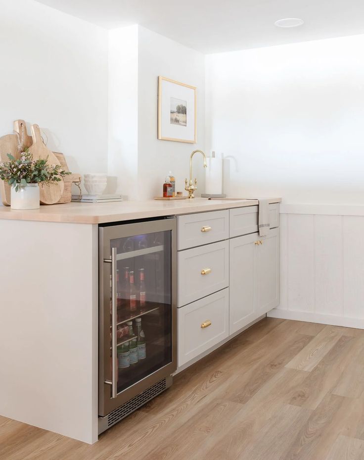 a kitchen with white cabinets and wood flooring has an icebox in the center