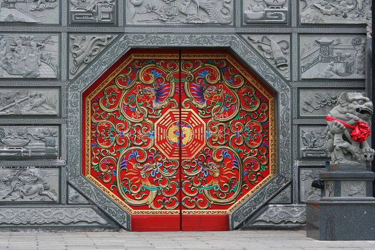 an intricately designed red door in front of a building with statues on either side