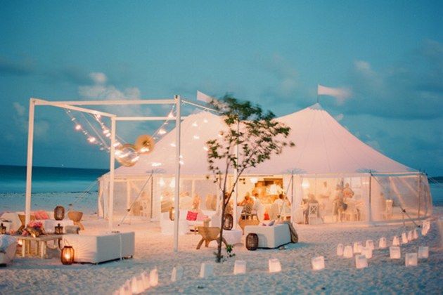 a tent set up on the beach for an outdoor wedding reception with white linens and candles