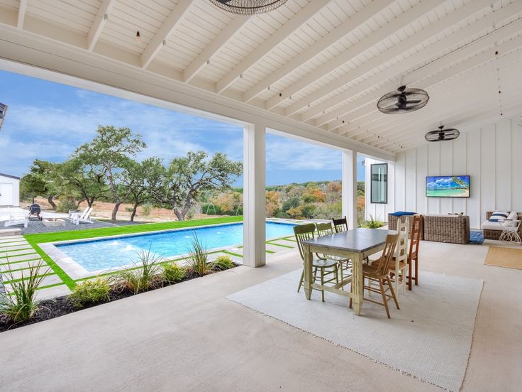 an outdoor living area with a pool and dining room table in the foreground, surrounded by white walls