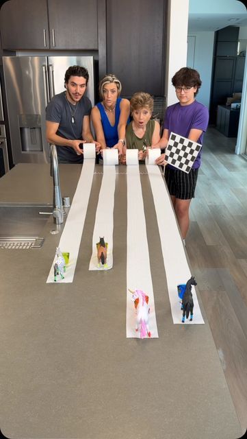 four people standing around a kitchen table with paper cutouts on the top and one person holding up a checkered flag