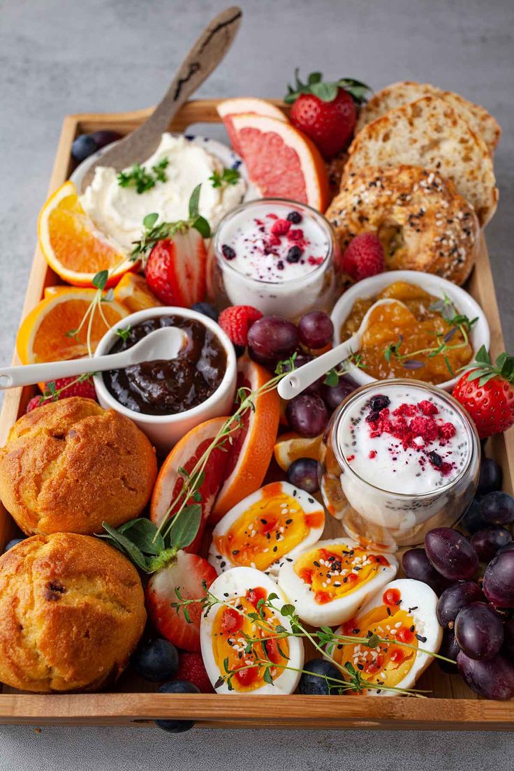 a wooden tray filled with fruit, bread and dips on top of a table