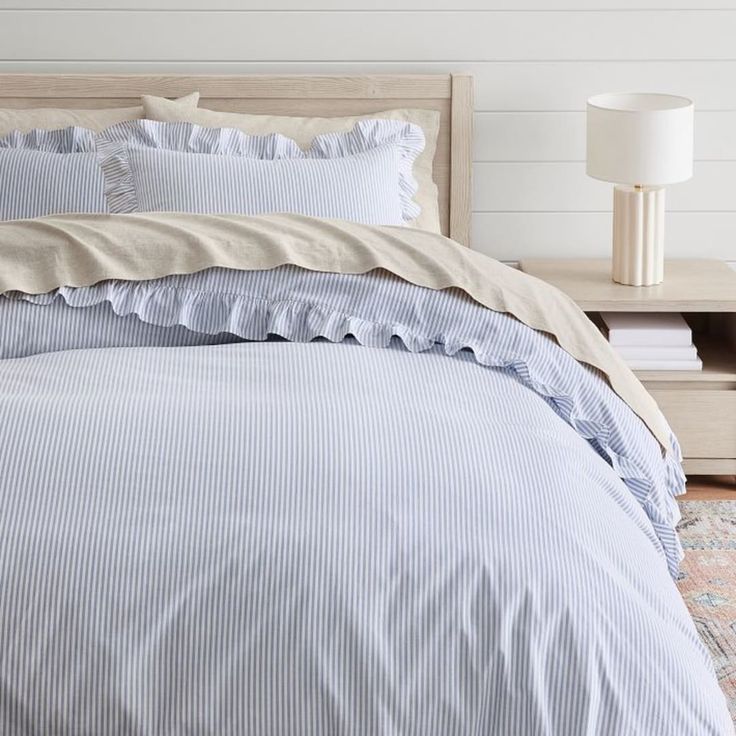 a bed with blue and white striped comforter next to a night stand on a rug