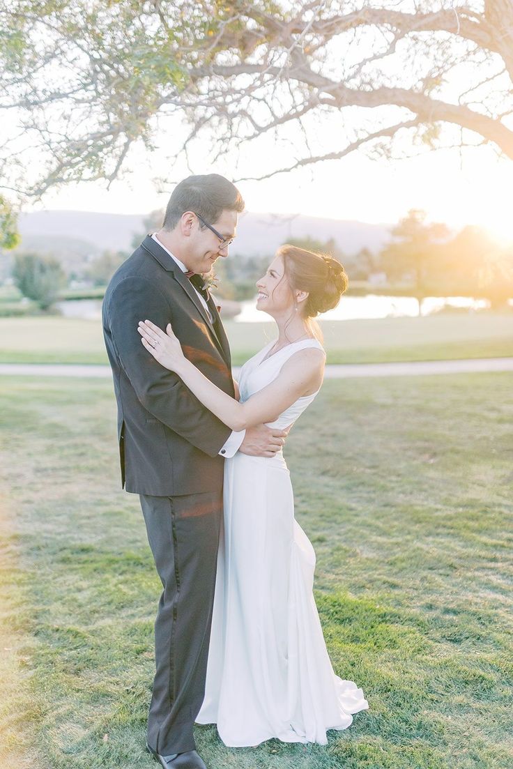 a bride and groom standing in the grass under a tree