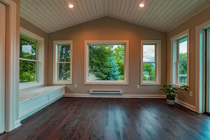 an empty room with wood flooring and three windows in the center, looking out onto trees