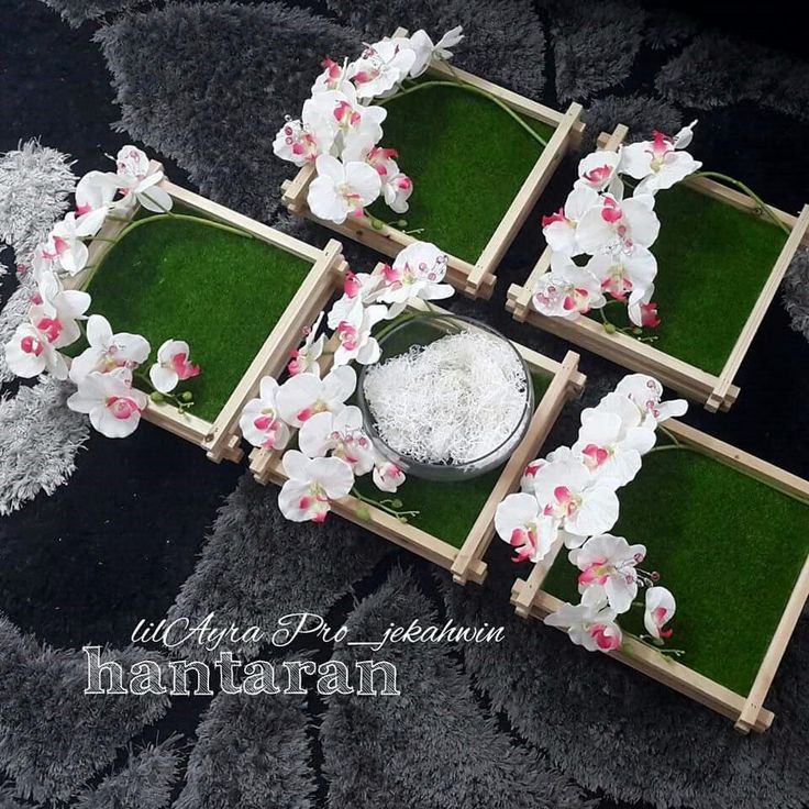 four small wooden trays with flowers and grass in them on a black table cloth