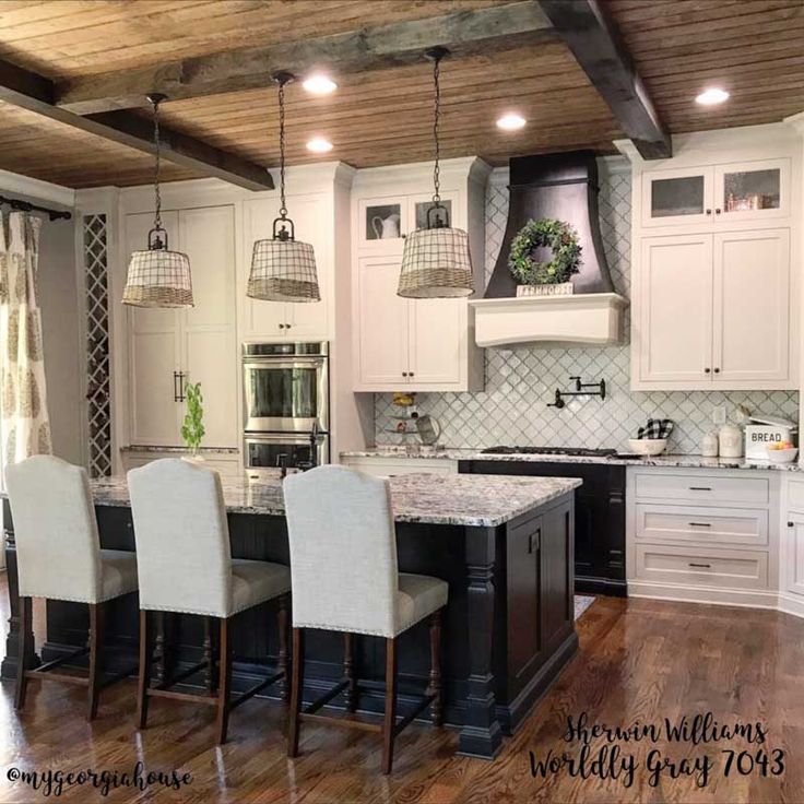 a large kitchen with white cabinets and black island in the center is decorated with hanging lights