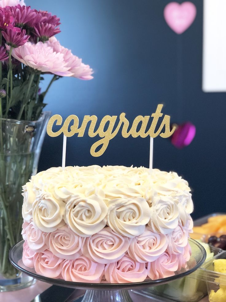 a cake that is sitting on a table with flowers in front of it and the words congrats written on top