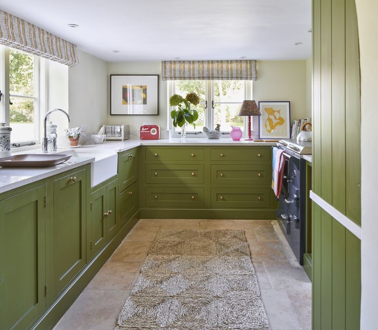 a kitchen with green cabinetry and white counter tops, along with an area rug on the floor