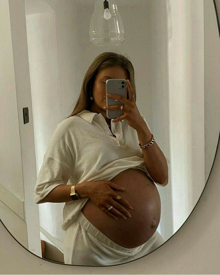 a pregnant woman taking a selfie in front of a mirror with her cell phone