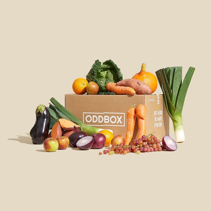 a cardboard box filled with assorted fruits and vegetables on top of a beige background