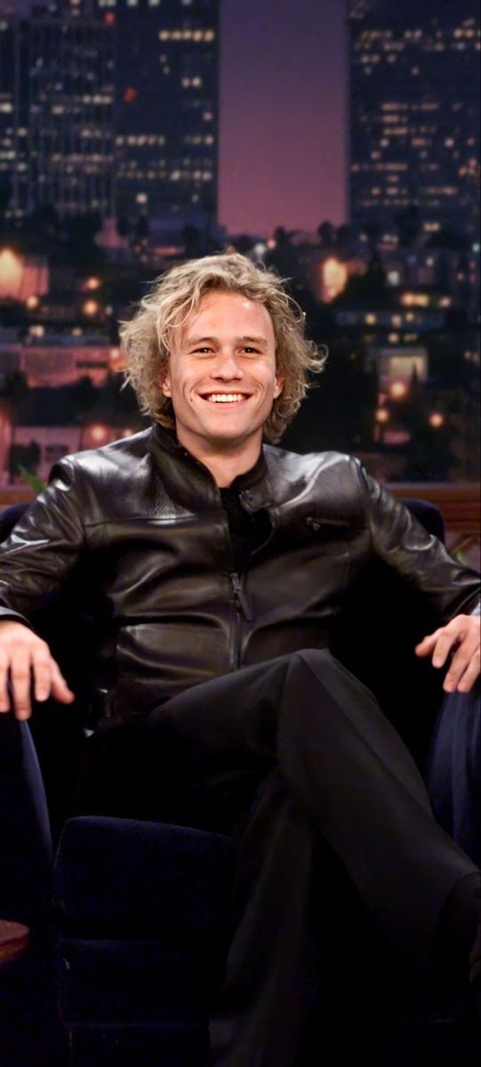 a man sitting in a chair with his legs crossed on the floor and wearing a black leather jacket