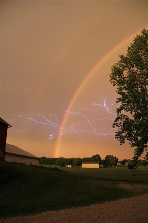 a double rainbow is seen in the sky over a house and tree with lightning coming from it