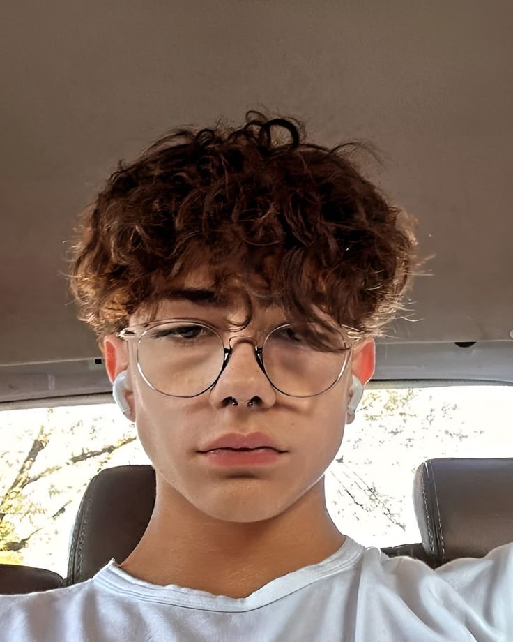 a young man wearing glasses sitting in the back seat of a car