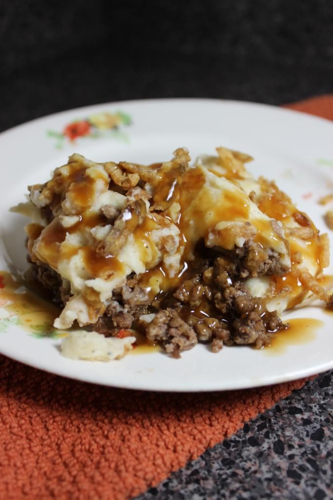 a white plate topped with meat and cheese covered in gravy on top of an orange towel