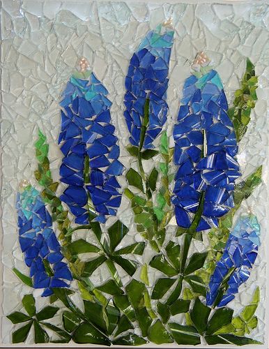 some blue flowers are in a vase on a mosaic tile wall hanging ornament