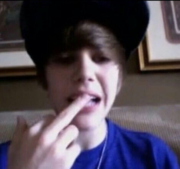 a young boy wearing a black hat and holding his finger up to his mouth while sitting on a couch