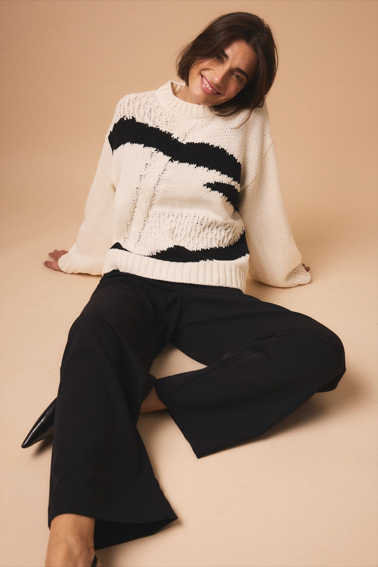 a woman sitting on the ground wearing black pants and a white sweater with stripes is smiling