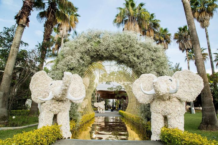 two elephants made out of flowers and plants in front of a garden archway with palm trees