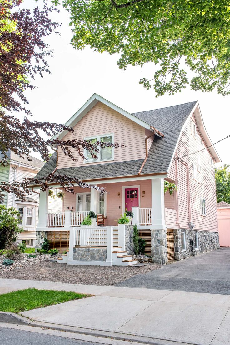 a pink house with white trim on the front porch and steps leading up to it