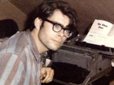 a man wearing glasses sitting in front of an old typewriter