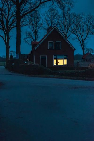 a red house sitting on the side of a road at night with its windows lit up