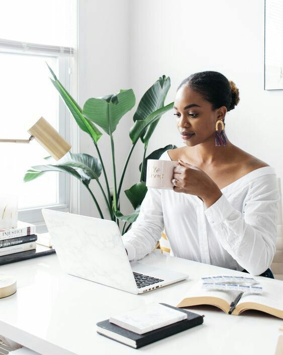 a woman sitting at a desk with a laptop and coffee in front of her,