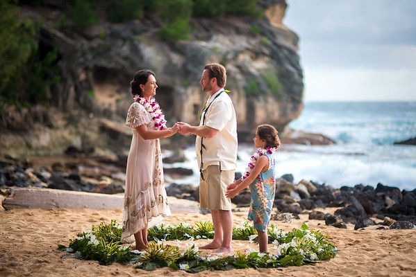 a man and woman holding hands while standing on the beach with two small children in front of them