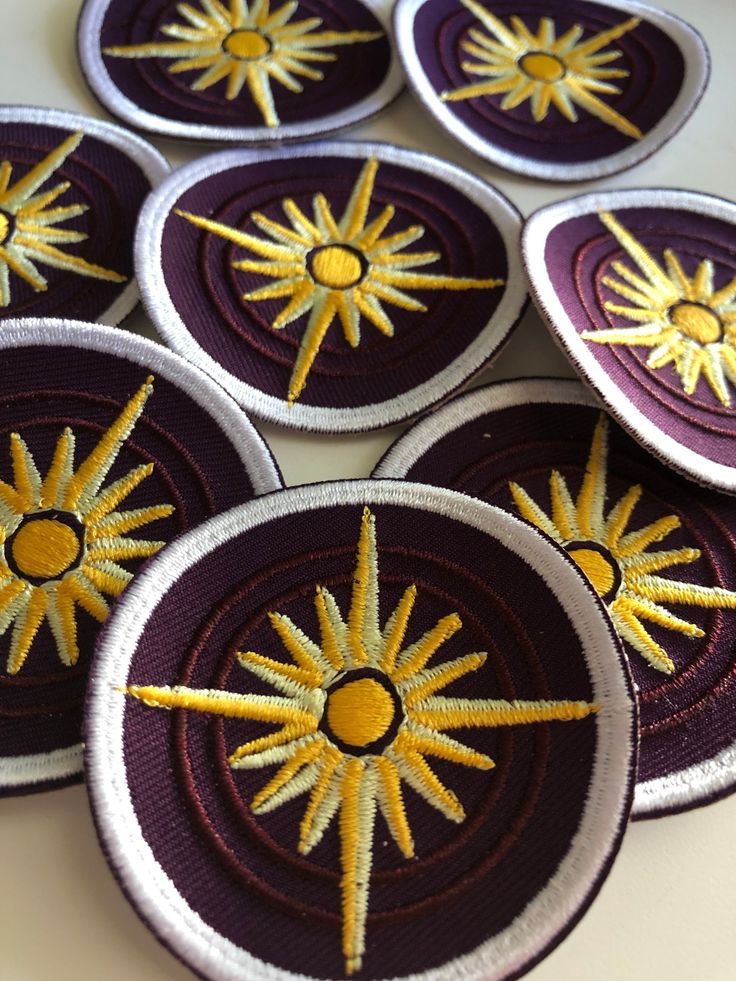 six purple and yellow embroidered badges with sun design on the front, set against a white background