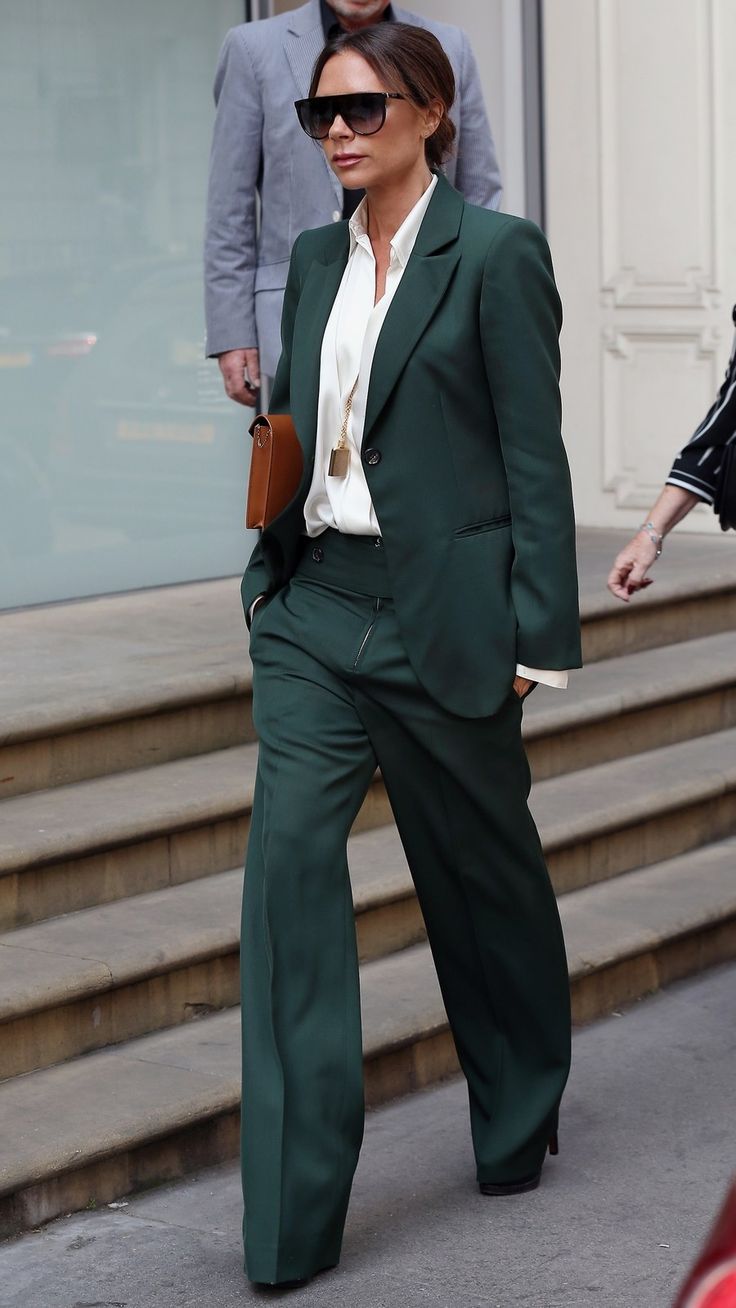 a woman in a green suit is walking down the street with her hand on her hip